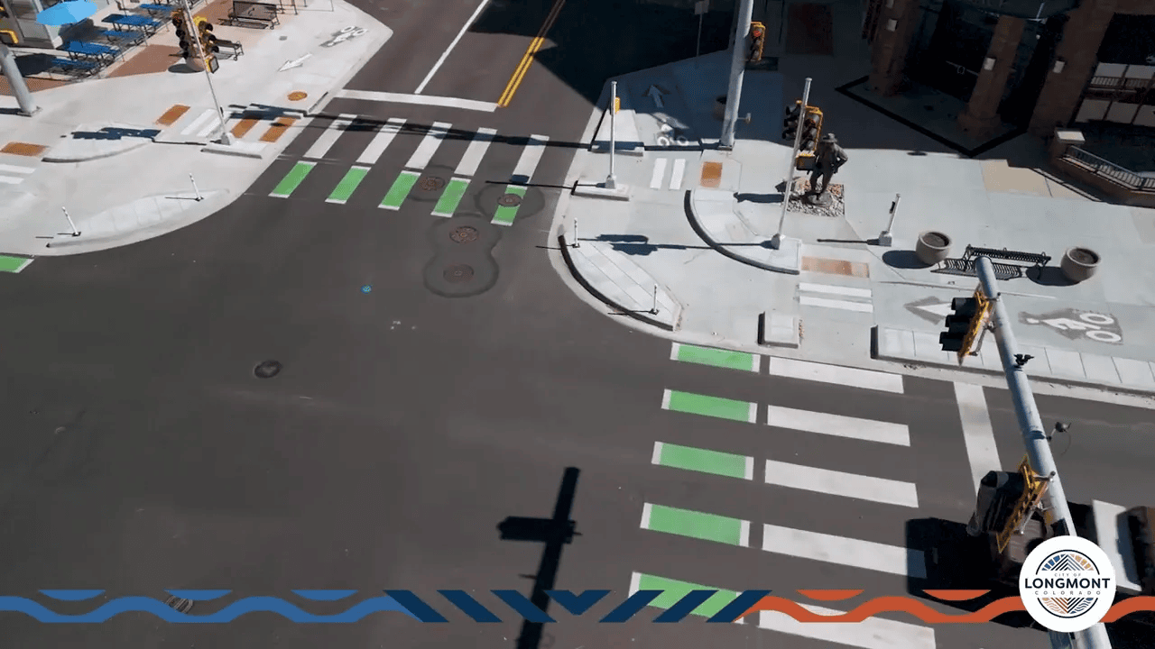 Aerial view of a protected intersection corner showing the corner island, shortened white pedestrian crosswalks, green bike crossing panels, tactile ramps and a clear sidewalk layout.