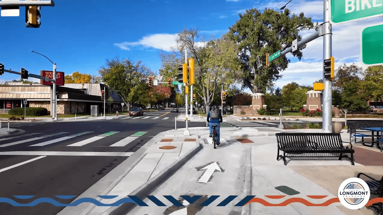 Cyclist riding in a setback bike lane into the bike waiting area at a protected intersection with arrow markings and corner island.