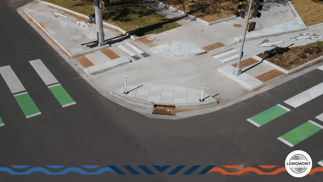 Close aerial shot of a corner island narrowing the turn radius with adjacent white crosswalks and green bike crossing markings.